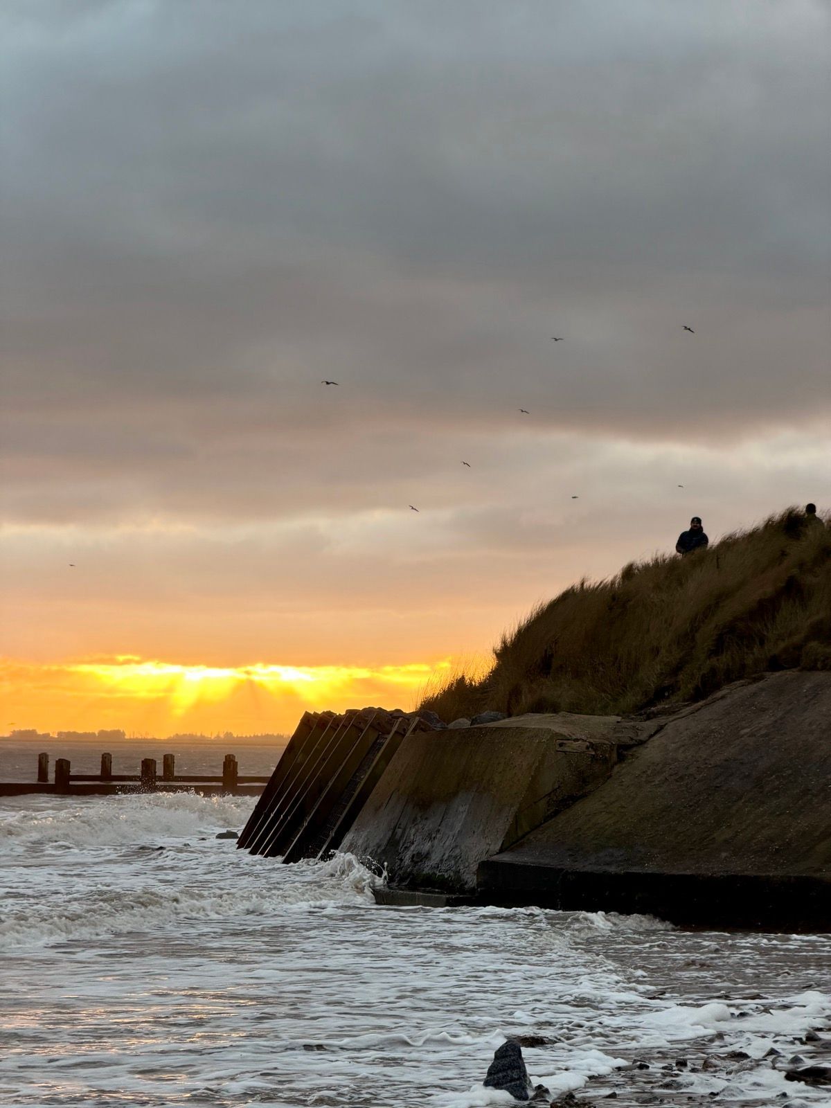 Sunrise light breaks beneath dark clouds over waves and dunes on Christmas Day.