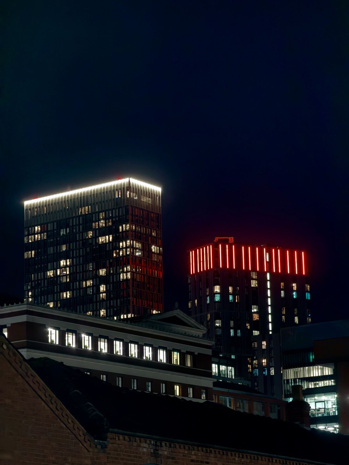 Two illuminated high-rise buildings at night above a brick rooftop in Birmingham.